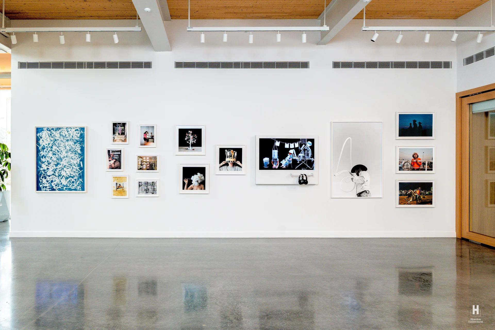 Bright modern gallery with a row of varied framed artworks and a digital display on a white wall, polished concrete floor reflecting.